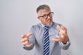 Hispanic business man with grey hair wearing glasses shouting frustrated with rage, hands trying to strangle, yelling mad Royalty Free Stock Photo