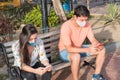 Hispanic couple in the park using the smartphone, wearing face masks and respecting social distancing during a pandemic