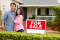 Hispanic couple satnding with a sign outside house