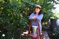 Hispanic cute woman gardener stands on ladder with a bucket full of freshly picked cherries for sale in farmers markets.