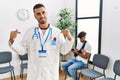 Hispanic doctor man at waiting room with pacient with arm injury looking confident with smile on face, pointing oneself with