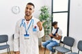 Hispanic doctor man at waiting room with pacient with arm injury smiling with happy face looking and pointing to the side with