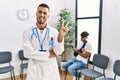 Hispanic doctor man at waiting room with pacient with arm injury smiling with happy face winking at the camera doing victory sign