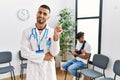 Hispanic doctor man at waiting room with pacient with arm injury smiling happy pointing with hand and finger to the side