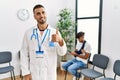 Hispanic doctor man at waiting room with pacient with arm injury smiling happy and positive, thumb up doing excellent and approval