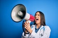 Hispanic doctor woman wearing medical white coat shouting angry on protest through megaphone Royalty Free Stock Photo