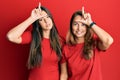 Hispanic family of mother and daughter wearing casual clothes over red background making fun of people with fingers on forehead