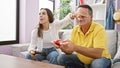 Hispanic father and daughter enjoy playing video game on the cozy home sofa, covering eyes and hands in laugh-filled skulduggery