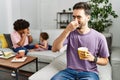 Hispanic father of interracial family drinking a cup coffee smelling something stinky and disgusting, intolerable smell, holding