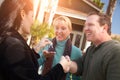 Hispanic Female Real Estate Agent Handing Over New House Keys to Happy Couple In Front of House