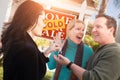 Hispanic Female Real Estate Agent Handing Over New House Keys to Happy Couple In Front of Sold For Sale Real Estate Sign