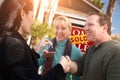 Hispanic Female Real Estate Agent Handing Over New House Keys to Happy Couple In Front of Sold For Sale Real Estate Sign Royalty Free Stock Photo