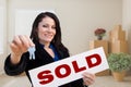 Hispanic Female Real Estate Agent with Sold Sign and Keys in Room with Moving Boxes. Royalty Free Stock Photo