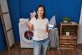 Hispanic girl with down syndrome ironing clothes at home winking looking at the camera with sexy expression, cheerful and happy Royalty Free Stock Photo