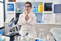 Hispanic girl with down syndrome working at scientist laboratory hands together and fingers crossed smiling relaxed and cheerful