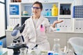 Hispanic girl with down syndrome working at scientist laboratory smiling cheerful presenting and pointing with palm of hand Royalty Free Stock Photo