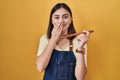 Hispanic girl eating healthy wooden spoon laughing and embarrassed giggle covering mouth with hands, gossip and scandal concept