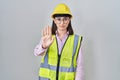 Hispanic girl wearing builder uniform and hardhat doing stop sing with palm of the hand Royalty Free Stock Photo