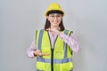 Hispanic girl wearing builder uniform and hardhat gesturing with hands showing big and large size sign, measure symbol