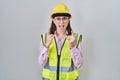 Hispanic girl wearing builder uniform and hardhat shouting with crazy expression doing rock symbol with hands up