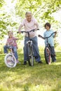 Hispanic Grandfather With Grandchildren In Park Riding Bikes