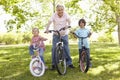 Hispanic Grandfather With Grandchildren In Park Riding Bikes