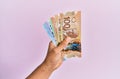 Hispanic hand holding canadian dollars banknotes over isolated pink background Royalty Free Stock Photo