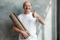 Hispanic male pensioner looking at camera while holding yoga mat in hands