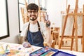 Hispanic man with beard at art studio showing and pointing up with fingers number two while smiling confident and happy Royalty Free Stock Photo