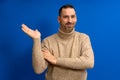 Hispanic man with beard and brown turtleneck sweater in skeptical attitude offering something in the palm of his hand Royalty Free Stock Photo