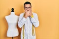 Hispanic man with beard dressmaker designer standing by manikin shocked covering mouth with hands for mistake Royalty Free Stock Photo