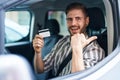 Hispanic Man With Beard Driving Car Holding Credit Card Pointing Thumb Up To The Side Smiling Happy With Open Mouth