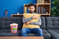 Hispanic man with beard eating popcorn watching a movie at home skeptic and nervous, frowning upset because of problem