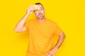 Hispanic man with beard in his 40s complaining about summer heat isolated on yellow background. Angry man wiping sweat