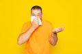 Hispanic man with beard in his 40s infected blowing his nose with a tissue because he is sick, isolated on yellow studio Royalty Free Stock Photo