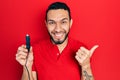 Hispanic Man With Beard Holding Car Charger Pointing Thumb Up To The Side Smiling Happy With Open Mouth