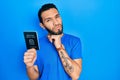 Hispanic man with beard holding italy passport with hand on chin thinking about question, pensive expression