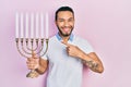 Hispanic man with beard holding menorah hanukkah jewish candle smiling happy pointing with hand and finger Royalty Free Stock Photo