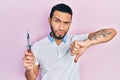 Hispanic man with beard holding pocket knife with angry face, negative sign showing dislike with thumbs down, rejection concept Royalty Free Stock Photo
