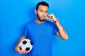 Hispanic man with beard holding soccer ball mouth and lips shut as zip with fingers