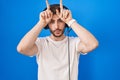 Hispanic man with beard listening to music wearing headphones doing funny gesture with finger over head as bull horns