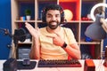 Hispanic man with beard playing video games with headphones amazed and smiling to the camera while presenting with hand and