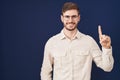 Hispanic man with beard standing over blue background showing and pointing up with finger number one while smiling confident and Royalty Free Stock Photo