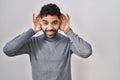 Hispanic man with beard standing over white background trying to hear both hands on ear gesture, curious for gossip Royalty Free Stock Photo