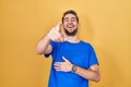 Hispanic man with beard standing over yellow background laughing at you, pointing finger to the camera with hand over body, shame Royalty Free Stock Photo