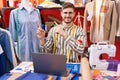 Hispanic man with beard using laptop at tailor room smiling and looking at the camera pointing with two hands and fingers to the