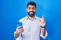 Hispanic man with beard using smartphone typing message gesturing finger crossed smiling with hope and eyes closed Royalty Free Stock Photo