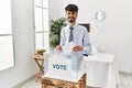 Hispanic man with beard voting putting envelop in ballot box with a happy and cool smile on face