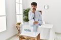 Hispanic man with beard voting putting envelop in ballot box looking at the camera blowing a kiss with hand on air being lovely