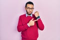Hispanic man with beard wearing business shirt and glasses in hurry pointing to watch time, impatience, looking at the camera with Royalty Free Stock Photo